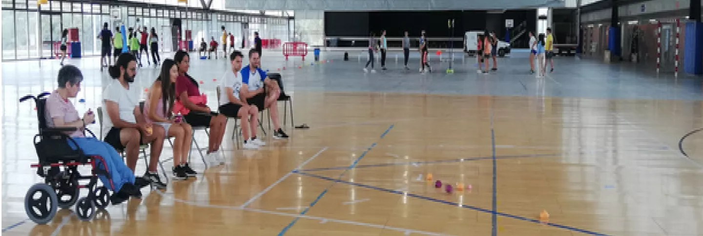 Grup de persones assegudes a cadires a l'esquerra de la foto en un poliesportiu